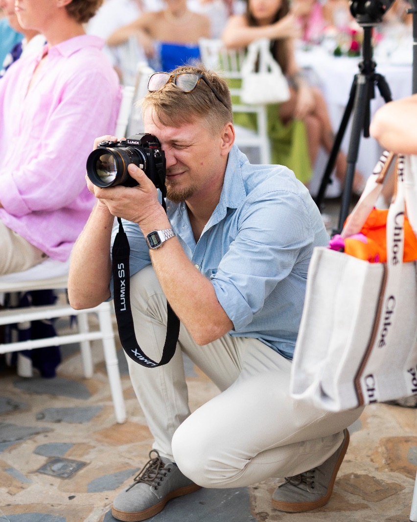 Niko, wedding videographer, crouching between guests to film at an outdoor wedding reception in Spain